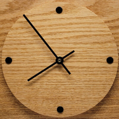 A square wall clock with round face, black arms and 4 black dots to indicate the time.