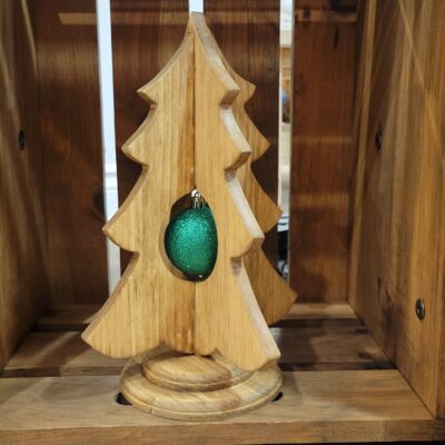 A rustic, simple wood christmas tree on a stand, with a green ornament inside the tree.