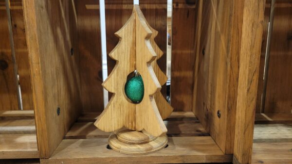 A rustic, simple wood christmas tree on a stand, with a green ornament inside the tree.