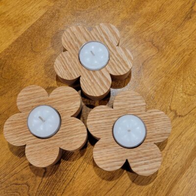 3 wooden flowers sitting on a table, with a white tealight nestled in the middle of each flower.