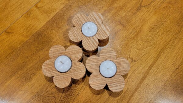 3 wooden flowers sitting on a table, with a white tealight nestled in the middle of each flower.