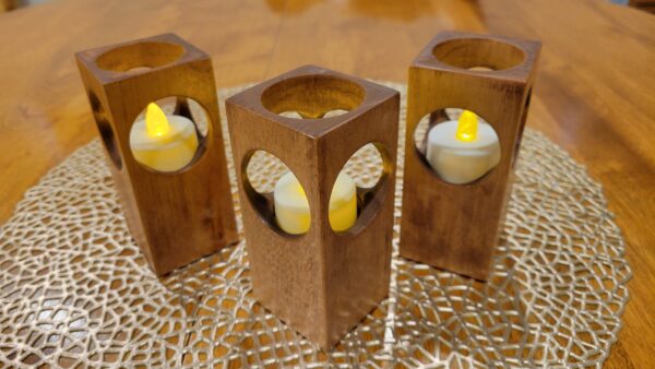 Three simple candle holders made from rectangular blocks of wood, with a hole on each of the four sides and the top. Flameless candles sit inside the blocks