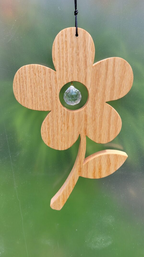 Wood flower with a glass prism ball suspended in the middle of the blossom, hanging in a window.