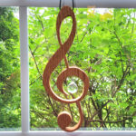 Wood treble clef that hangs in a window with a glass ball prism inset in the middle.