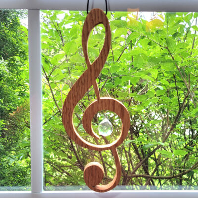 Wood treble clef that hangs in a window with a glass ball prism inset in the middle.