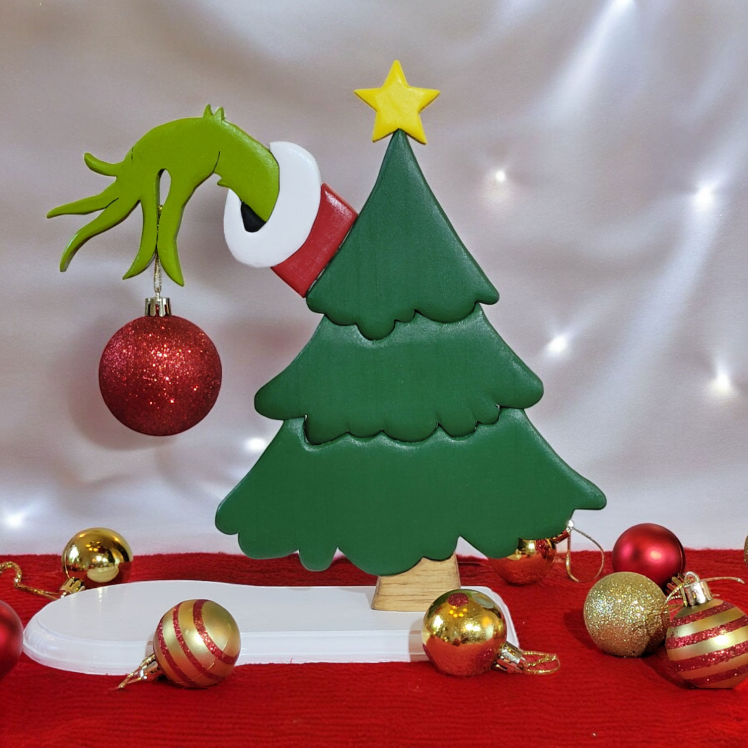 a green christmas tree with the hand of the Grinch, reaching out from behind, holding a red ornament.