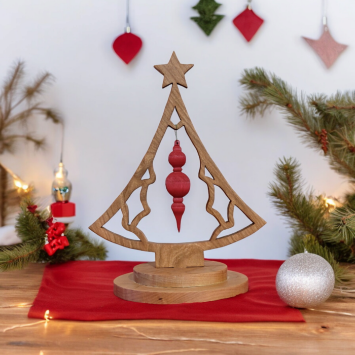 A delicate, scroll cut christmas tree sitting on a table top. The tree is shaped like a bell with a star on top. In the middle of the tree, a red ornament hangs.