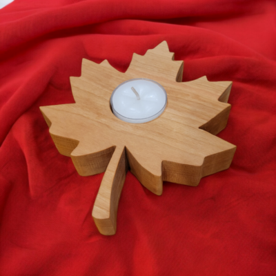 A solid wood, maple leaf shaped candle holder sits on a red fabric surface. It has a tealight nestled in the middle of the leaf.