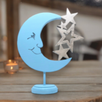 A wooden cutout of a partial light blue moon, connected to 4 silver stars. The moon has a cheerful smiling face.