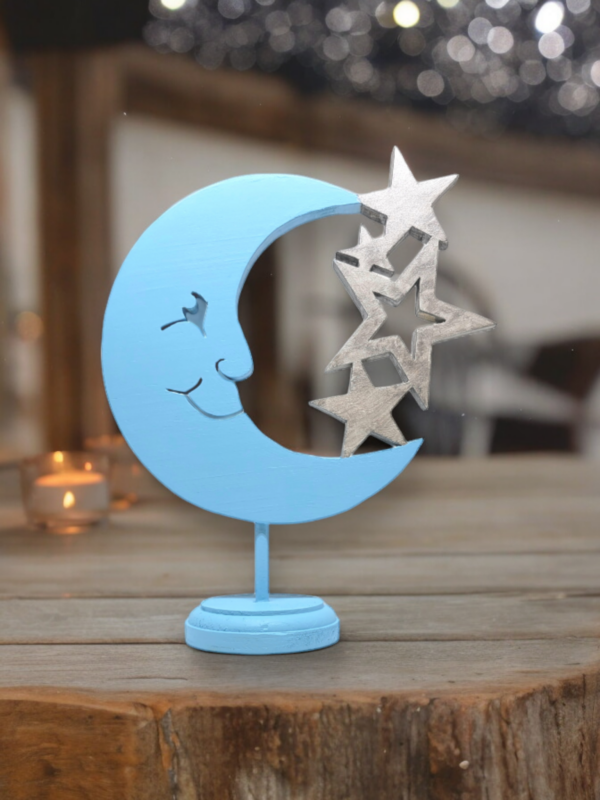 A wooden cutout of a partial light blue moon, connected to 4 silver stars. The moon has a cheerful smiling face.