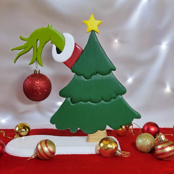 a green christmas tree with the hand of the Grinch, reaching out from behind, holding a red ornament.