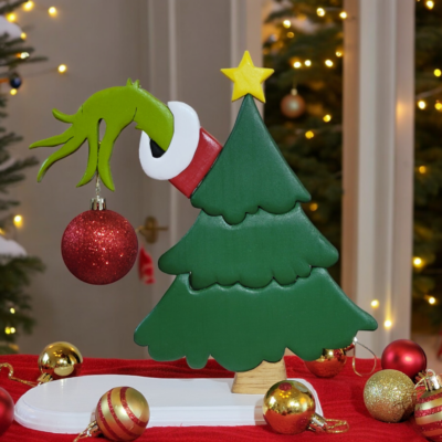 a green christmas tree with the hand of the Grinch, reaching out from behind, holding a red ornament.