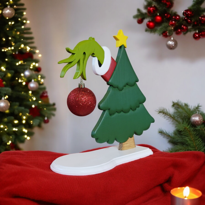 a green christmas tree with the hand of the Grinch, reaching out from behind, holding a red ornament.