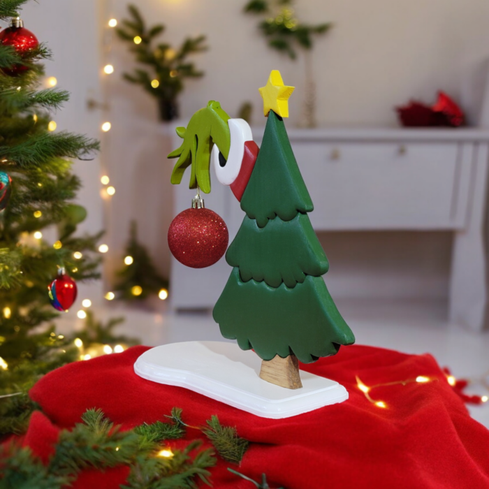 a green christmas tree with the hand of the Grinch, reaching out from behind, holding a red ornament.