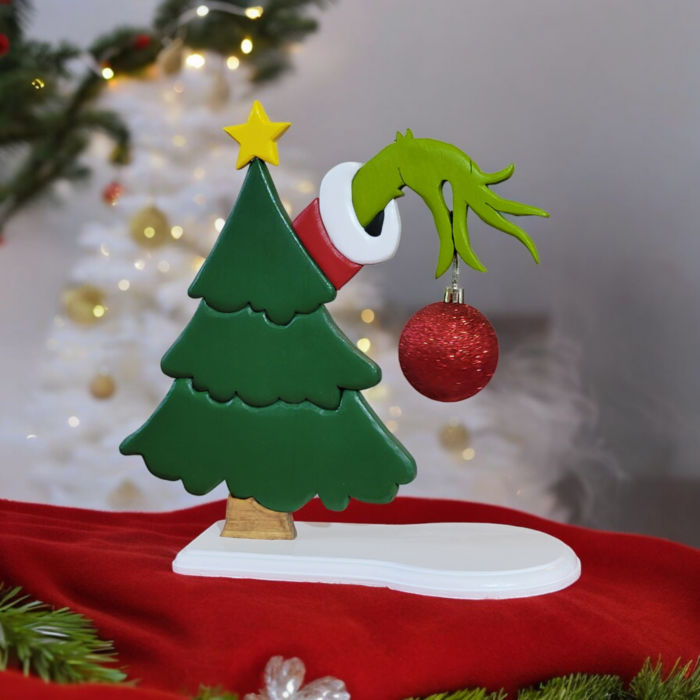 a green christmas tree with the hand of the Grinch, reaching out from behind, holding a red ornament.