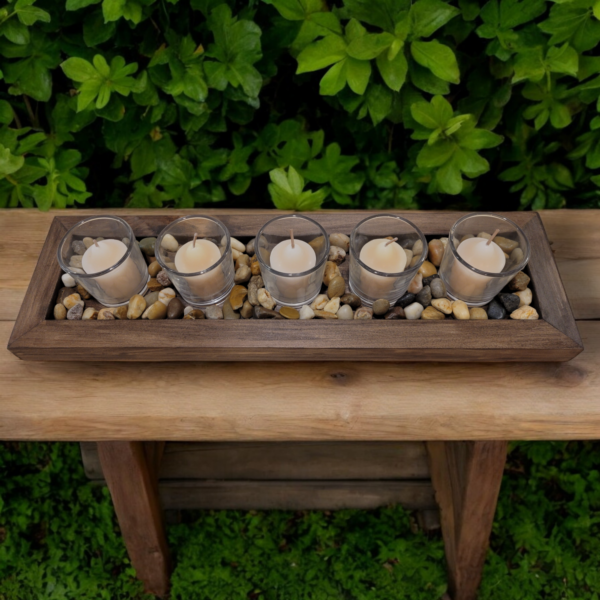 A simple rectangular wooden tray, covered with small smooth stones. Nestled among the stones are five glass votive candle holders.