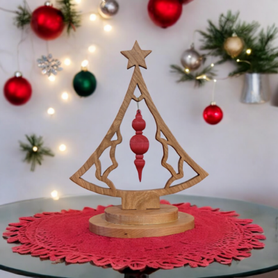 A delicate, scroll cut christmas tree sitting on a table top. The tree is shaped like a bell with a star on top. In the middle of the tree, a red ornament hangs.