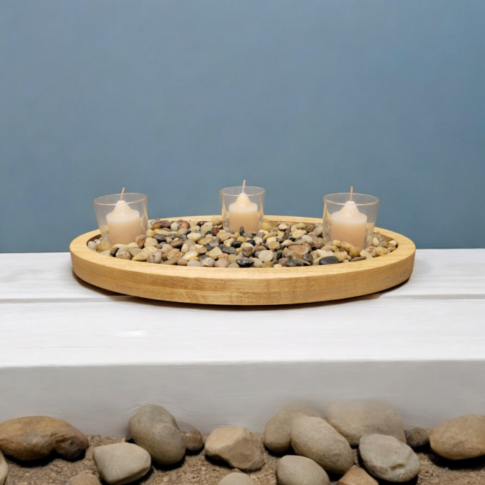 A simple oval wooden tray, covered with small smooth stones. Nestled among the stones are three glass votive candle holders.