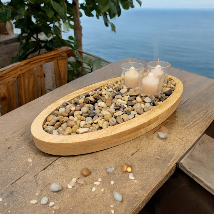 A simple oval wooden tray, covered with small smooth stones. Nestled among the stones are three glass votive candle holders.