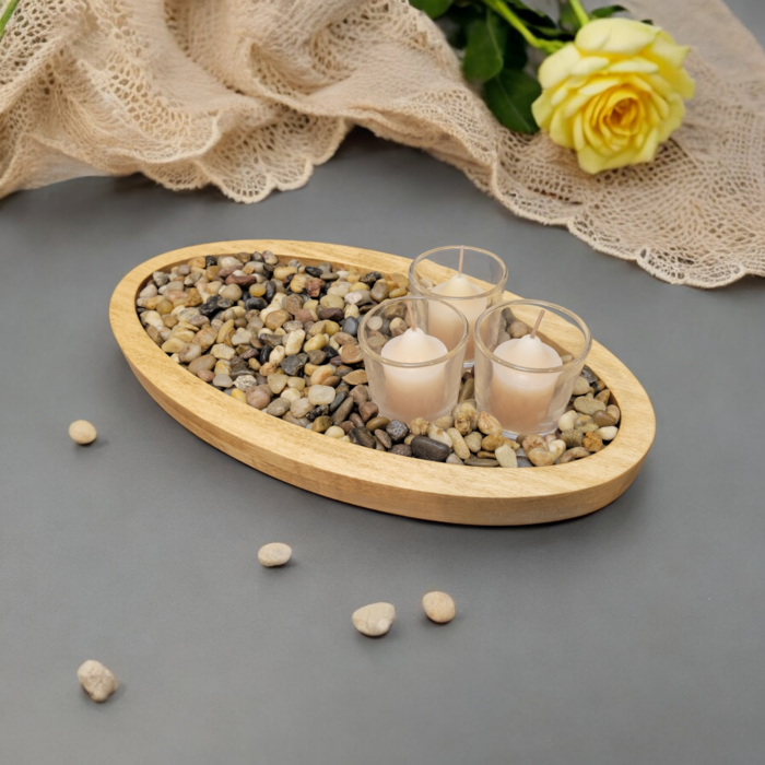 A simple oval wooden tray, covered with small smooth stones. Nestled among the stones are three glass votive candle holders.