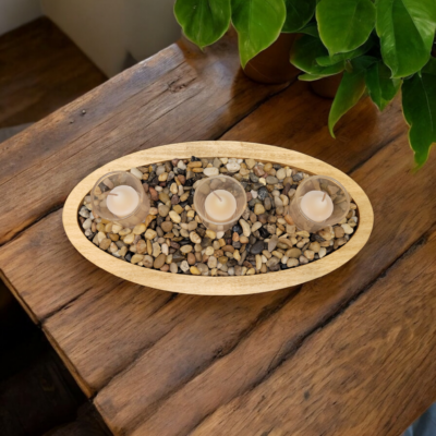 A simple oval wooden tray, covered with small smooth stones. Nestled among the stones are three glass votive candle holders.