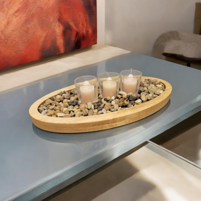 A simple oval wooden tray, covered with small smooth stones. Nestled among the stones are three glass votive candle holders.