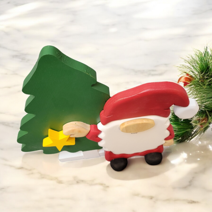 Christmas gnome with while beard, red hat, holding a yellow star, standing in front of a tall green tree.