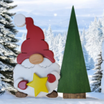 Christmas gnome with while beard, red hat and gloves, holding a yellow star, standing in front of a tall green tree.