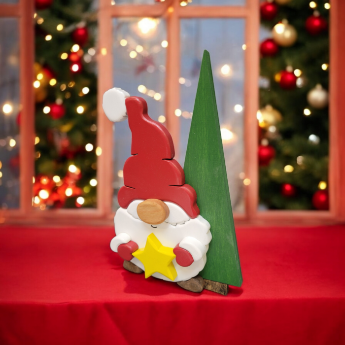 Christmas gnome with while beard, red hat and gloves, holding a yellow star, standing in front of a tall green tree.