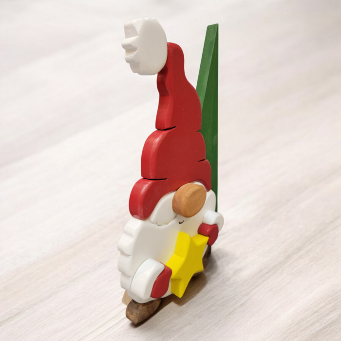 Christmas gnome with while beard, red hat and gloves, holding a yellow star, standing in front of a tall green tree.