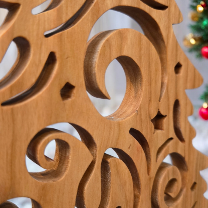 A delicate and intricately cut christmas tree sits on a table. The tree has curves and swirls cut into it, giving it a look of swirling wind.