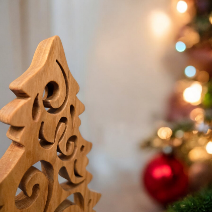 A delicate and intricately cut christmas tree sits on a table. The tree has curves and swirls cut into it, giving it a look of swirling wind.