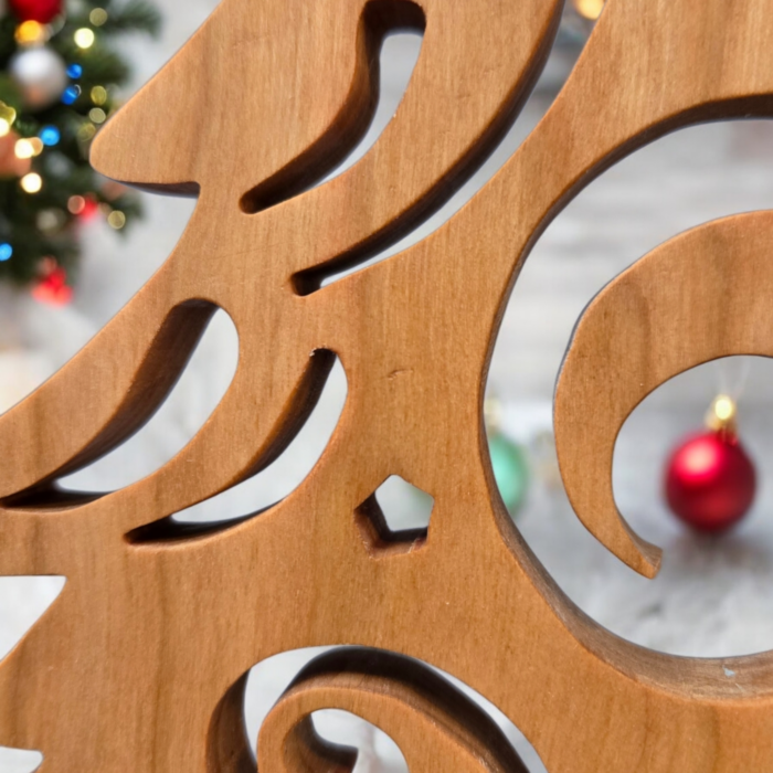 A delicate and intricately cut christmas tree sits on a table. The tree has curves and swirls cut into it, giving it a look of swirling wind.