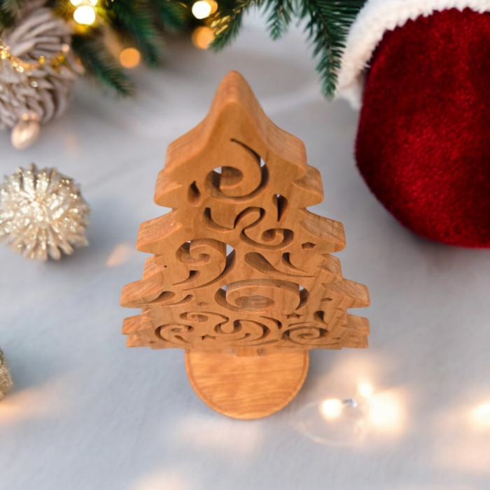 A delicate and intricately cut christmas tree sits on a table. The tree has curves and swirls cut into it, giving it a look of swirling wind.