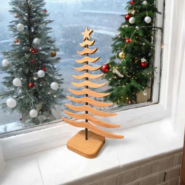 Wooden tree sitting on a white window ledge, with decorated christmas trees outside the window.