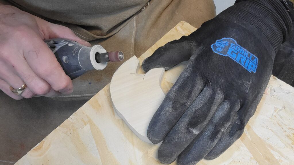 Photo of a person using a Dremel rotary tool, to sand and shape a piece of wood.