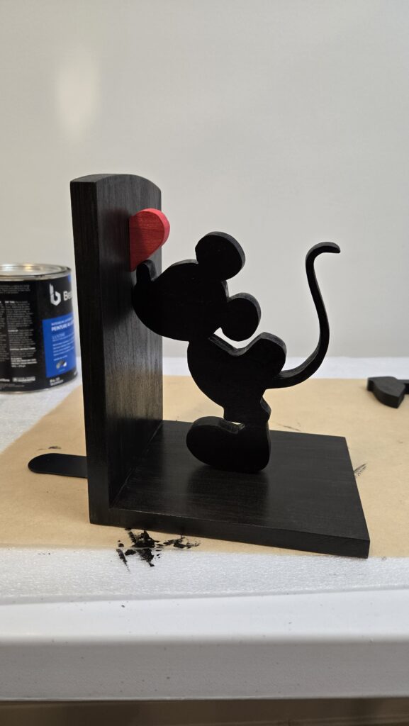 A black wood bookend with Mickey Mouse kissing the upright end, and a red heart above.  Minnie, not shown, is on the opposite side.