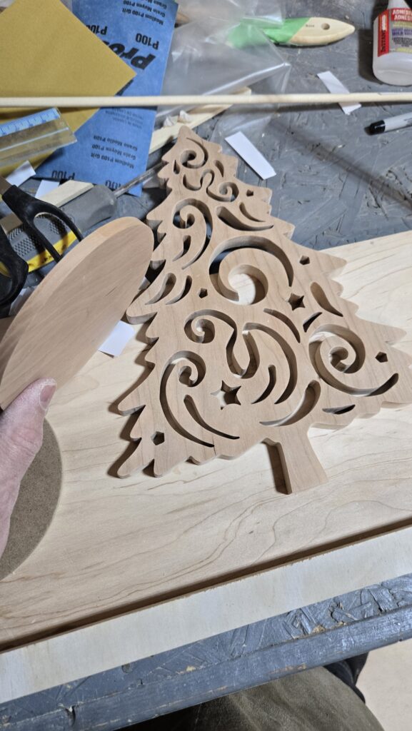 A wood Christmas tree with curved cutouts, lying on the workbench, ready to be finished.