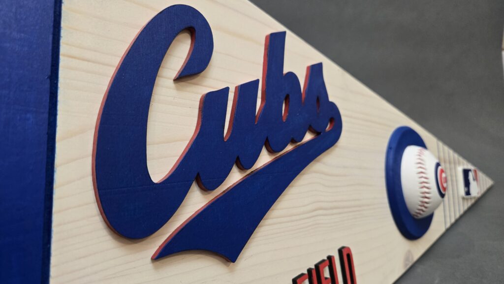 The Chicago Cubs logo affixed to a wooden triangular pennant.  A baseball also rests in the middle of the pennant.