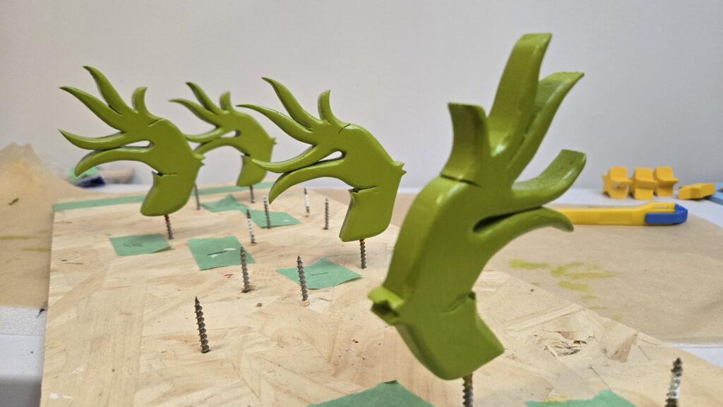 Green grinch hands, standing upright on the tips of wood screws, drying after being painted green.