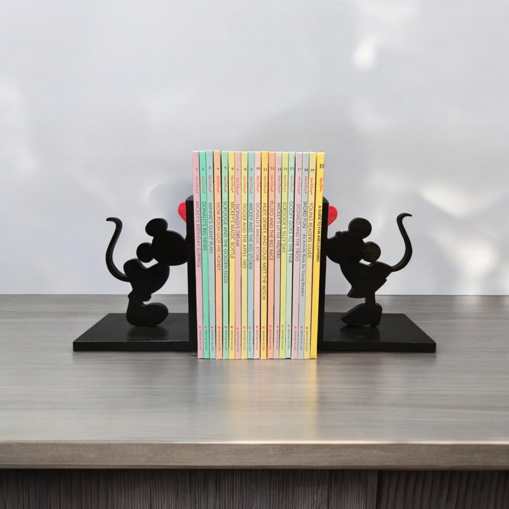 Photo of Mickey and Minnie Mouse bookends, holding books in the centre.  On one end stands Mickey and on the other, stand Minnie.  They appear to be kissing, and there is a heart above each of them.