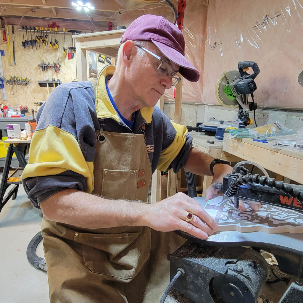 Shop owner, Michael, cutting out a wooden christmas tree, using a scroll saw.